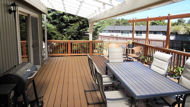 Una terraza cubierta al aire libre con una mesa, sillas, una parrilla y una estructura de pérgola.