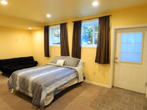 A bedroom with a bed, a couch, a window with curtains, and a door.
