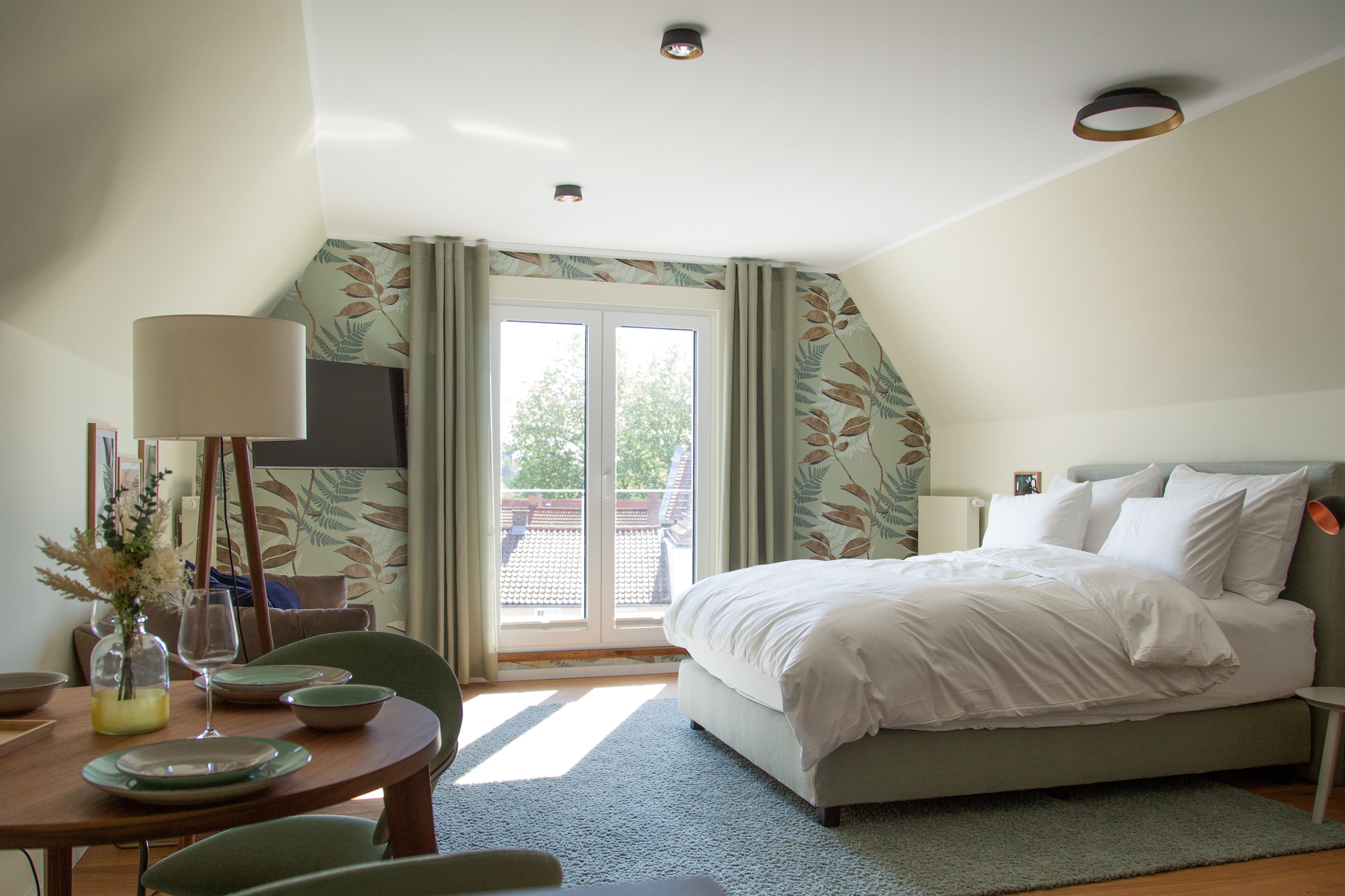 A bedroom with a bed, a dining table with chairs, and a view of the outdoors through a sliding door.