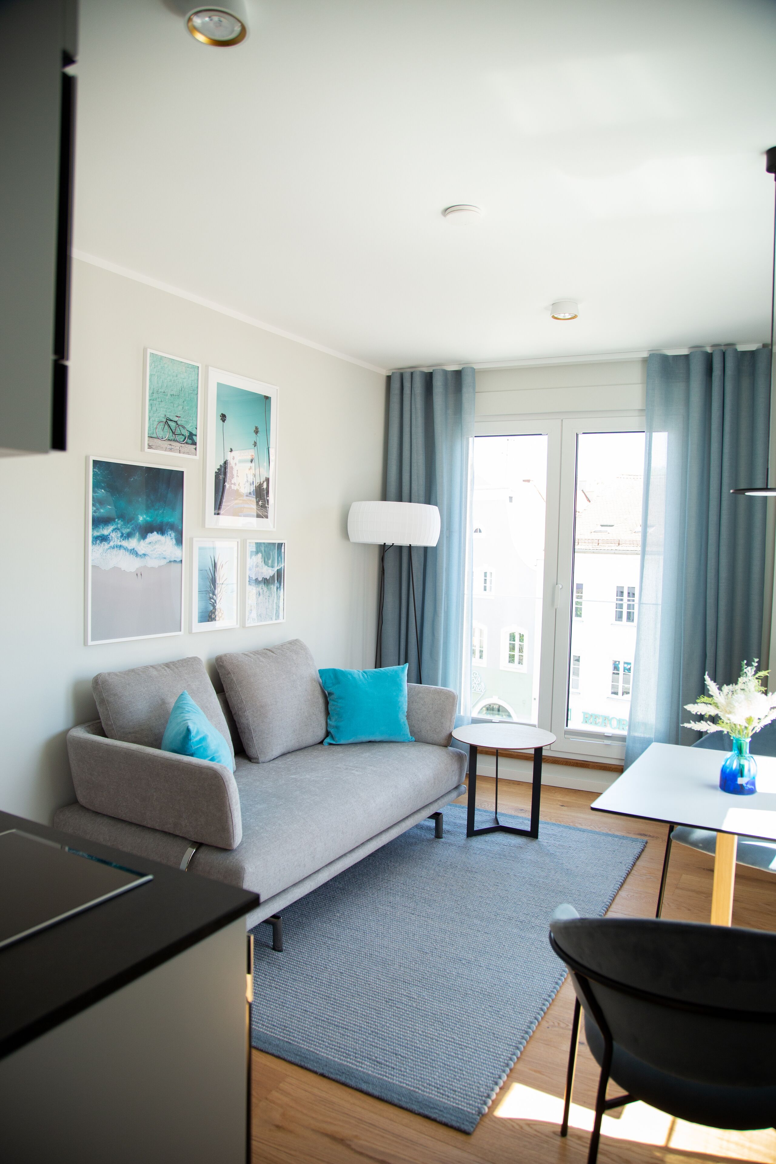 A modern living room with a grey sofa, a small round table, and a dining area.
