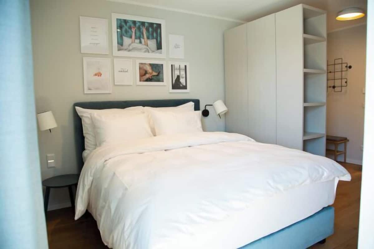 A bedroom with a bed, bedside tables, wall art, and a wardrobe.