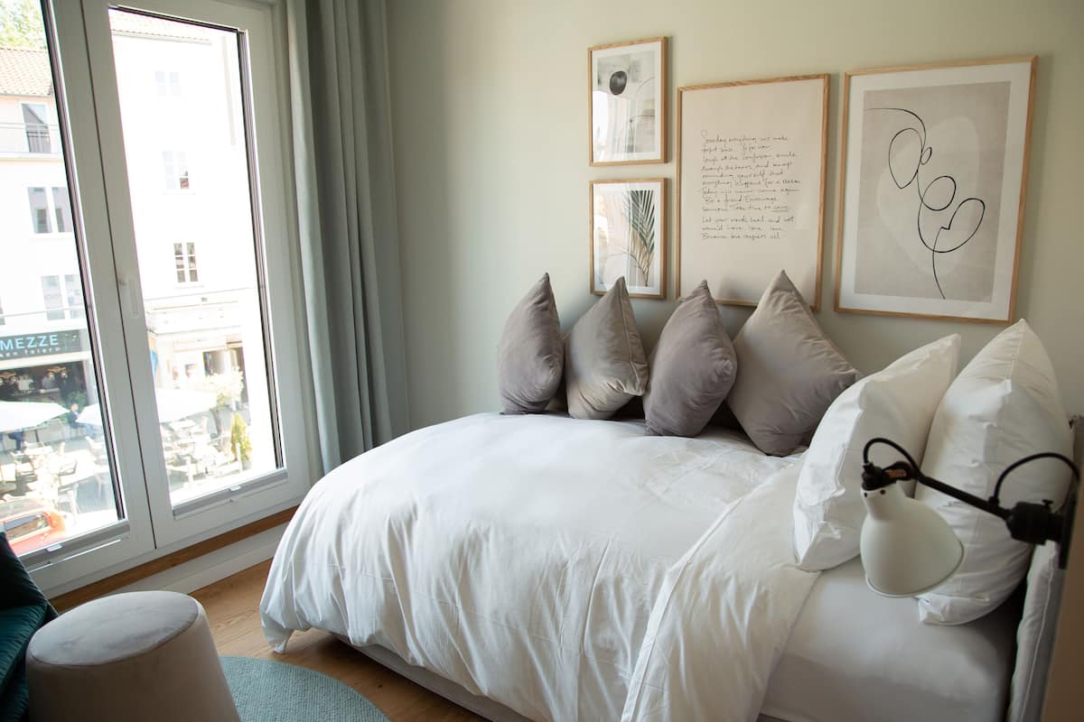 A bedroom with a bed, pillows, a bedside lamp, and artwork on the wall.