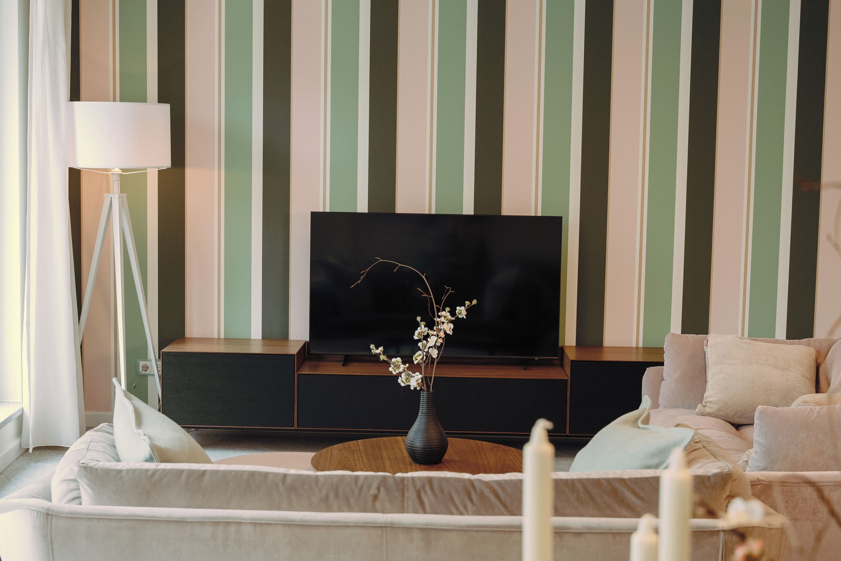 A living room with a TV on a stand, a vase with flowers, a lamp, and a sofa.