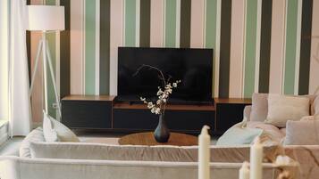 A living room with a TV on a stand, a vase with flowers, a lamp, and a sofa.