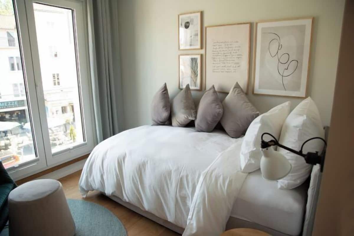 A bedroom with a bed, pillows, a lamp, and framed artwork on the wall.