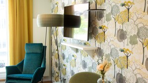 Uma sala de estar moderna com uma poltrona azul-turquesa, uma mesa redonda com um vaso de flores e um papel de parede estampado.