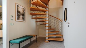 Una escalera de caracol con escalones de madera y barandillas de metal, un banco y un cuadro en la pared.