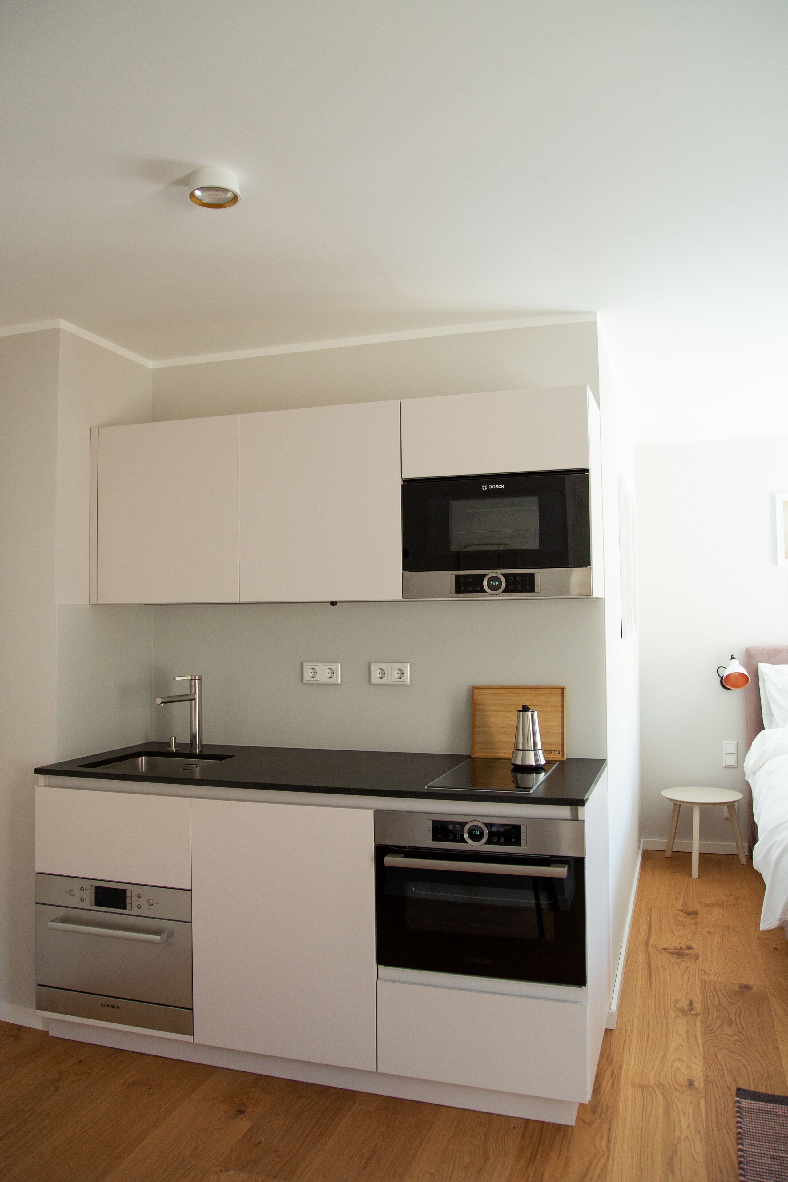 A compact kitchen with white cabinetry, a Bosch microwave, a coffee maker, and a built-in oven.