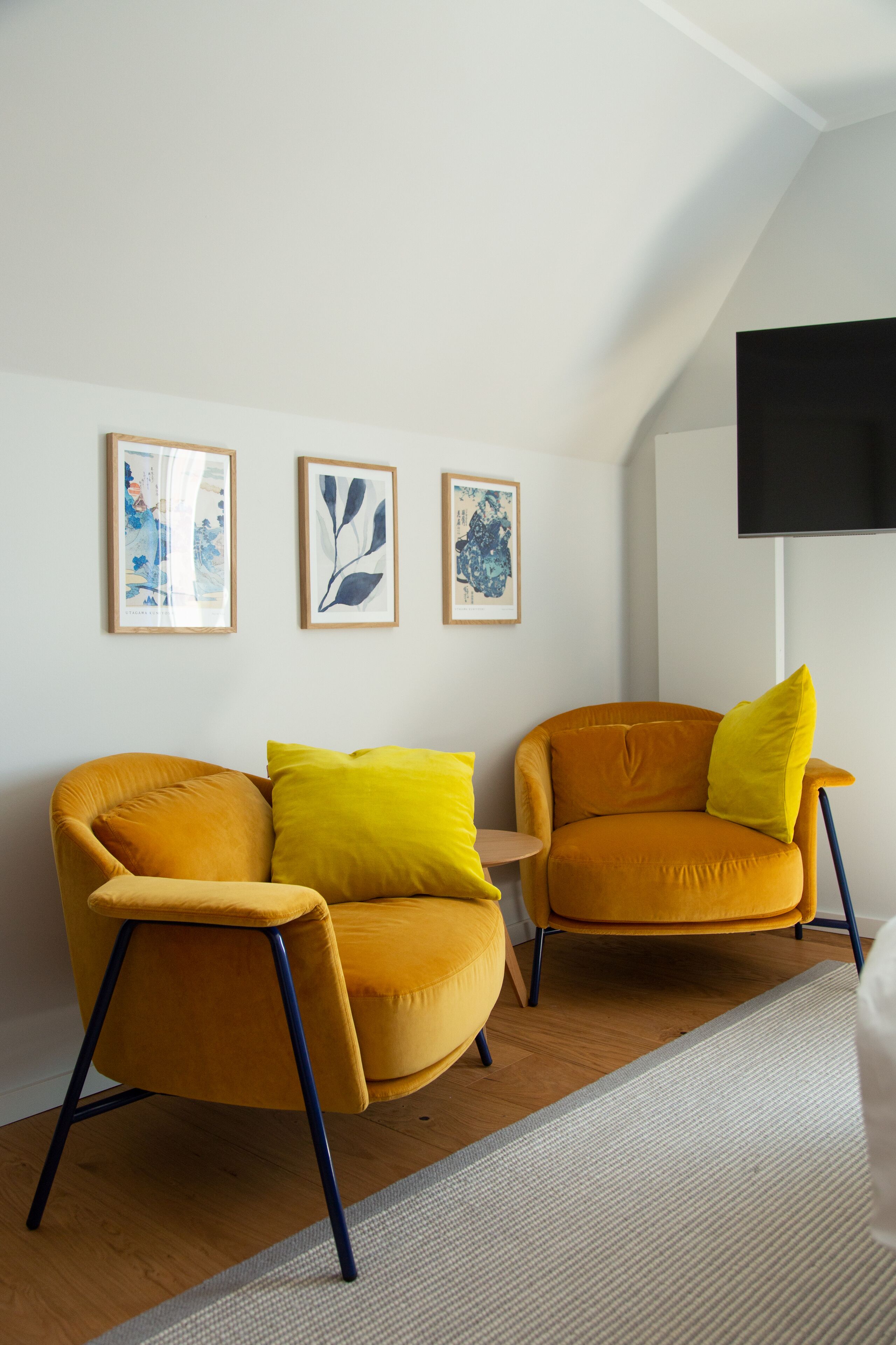 Ein Zimmer mit zwei gelben Sesseln, einem kleinen runden Tisch und drei gerahmten Kunstwerken an der Wand.
