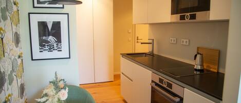 A compact kitchen with a microwave, oven, and sink. There is a framed picture on the wall and a vase with flowers on a table.