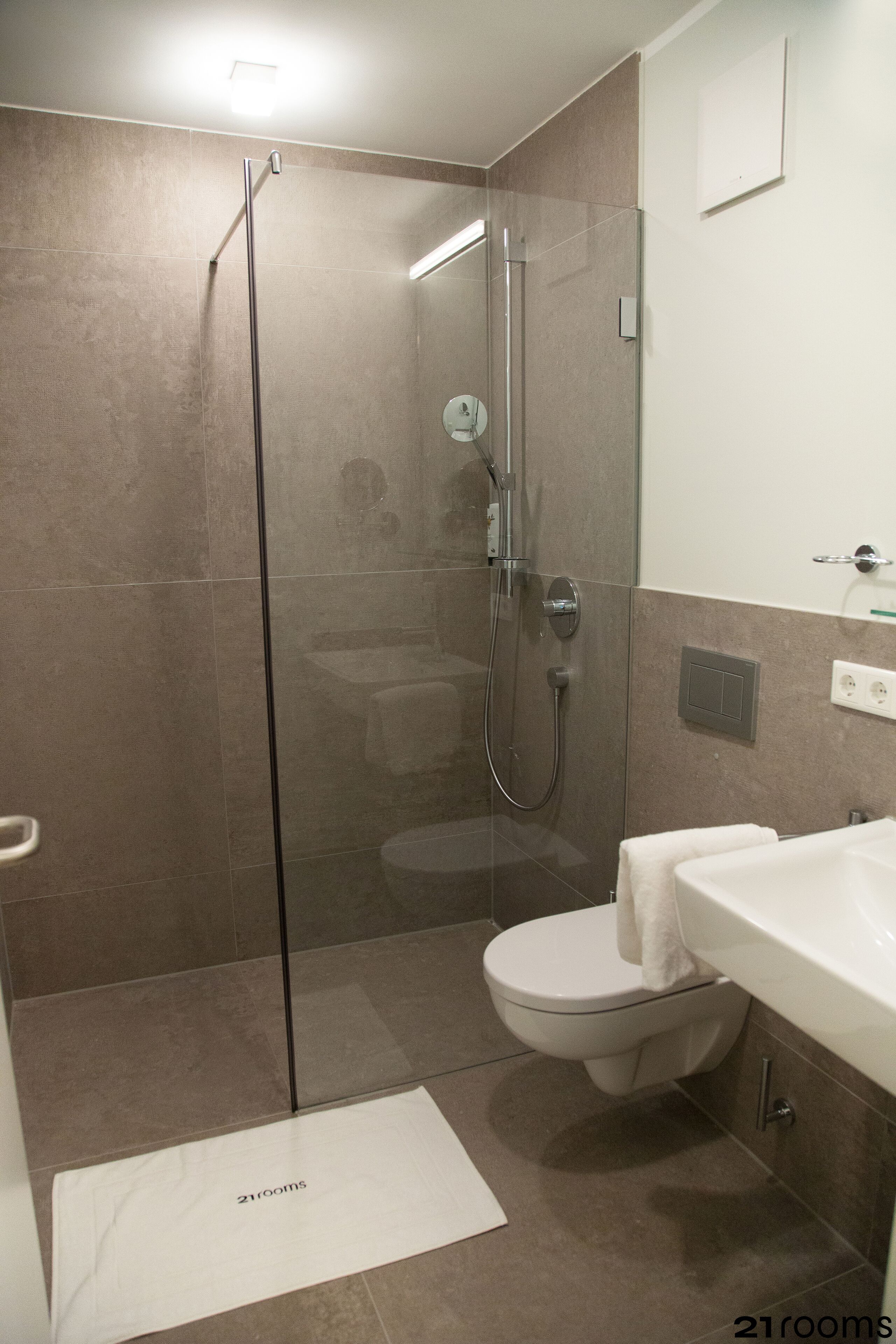 A modern bathroom with a glass-enclosed shower, a white toilet, and a sink with a towel.
