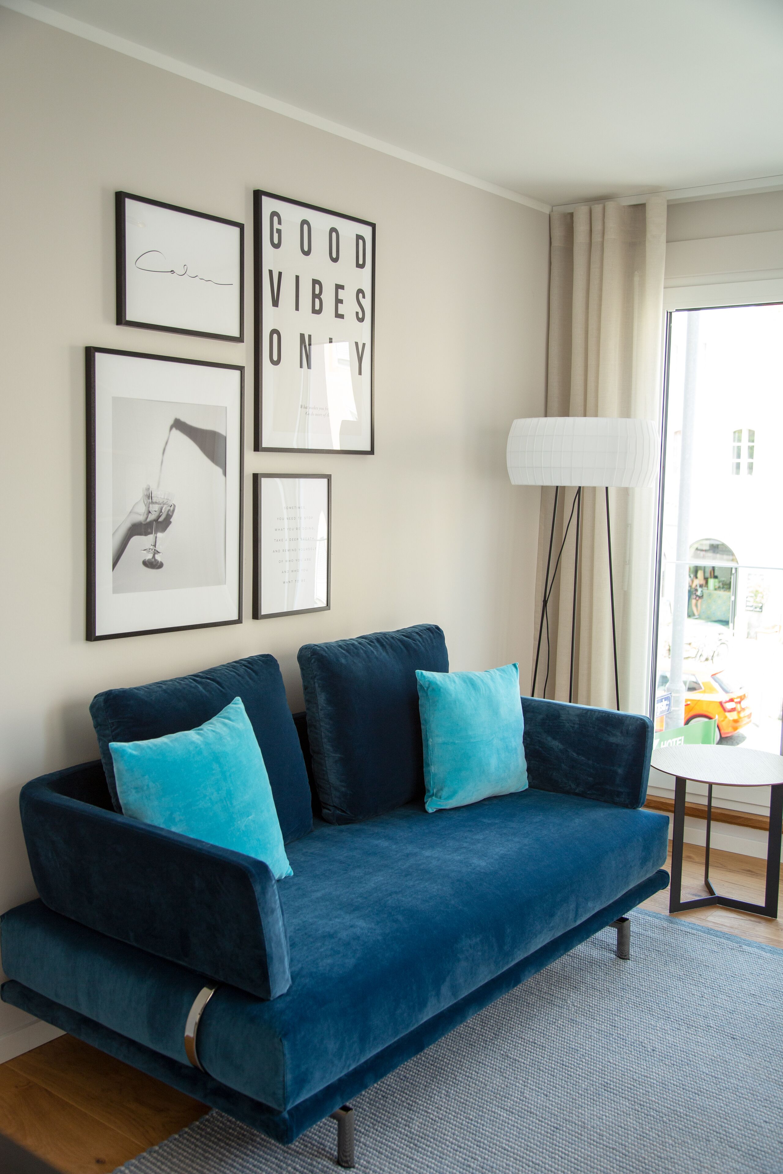 A modern living room with a dark blue sofa, teal cushions, and framed artwork on the wall.