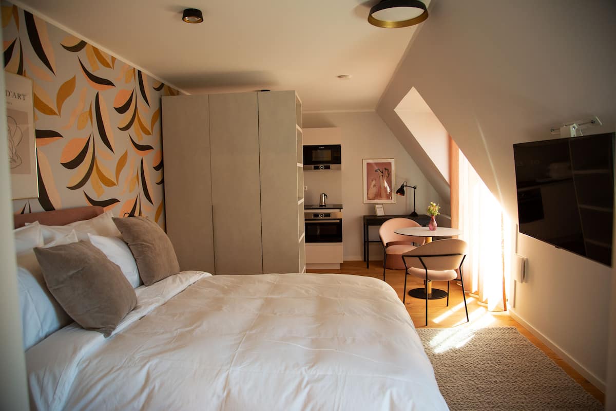 A modern bedroom with a large bed, a wardrobe, a kitchenette, and a dining area.