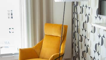 Una sala de estar moderna con un sillón amarillo, un otoman rojo, una lámpara de pie y una pared con estampado.