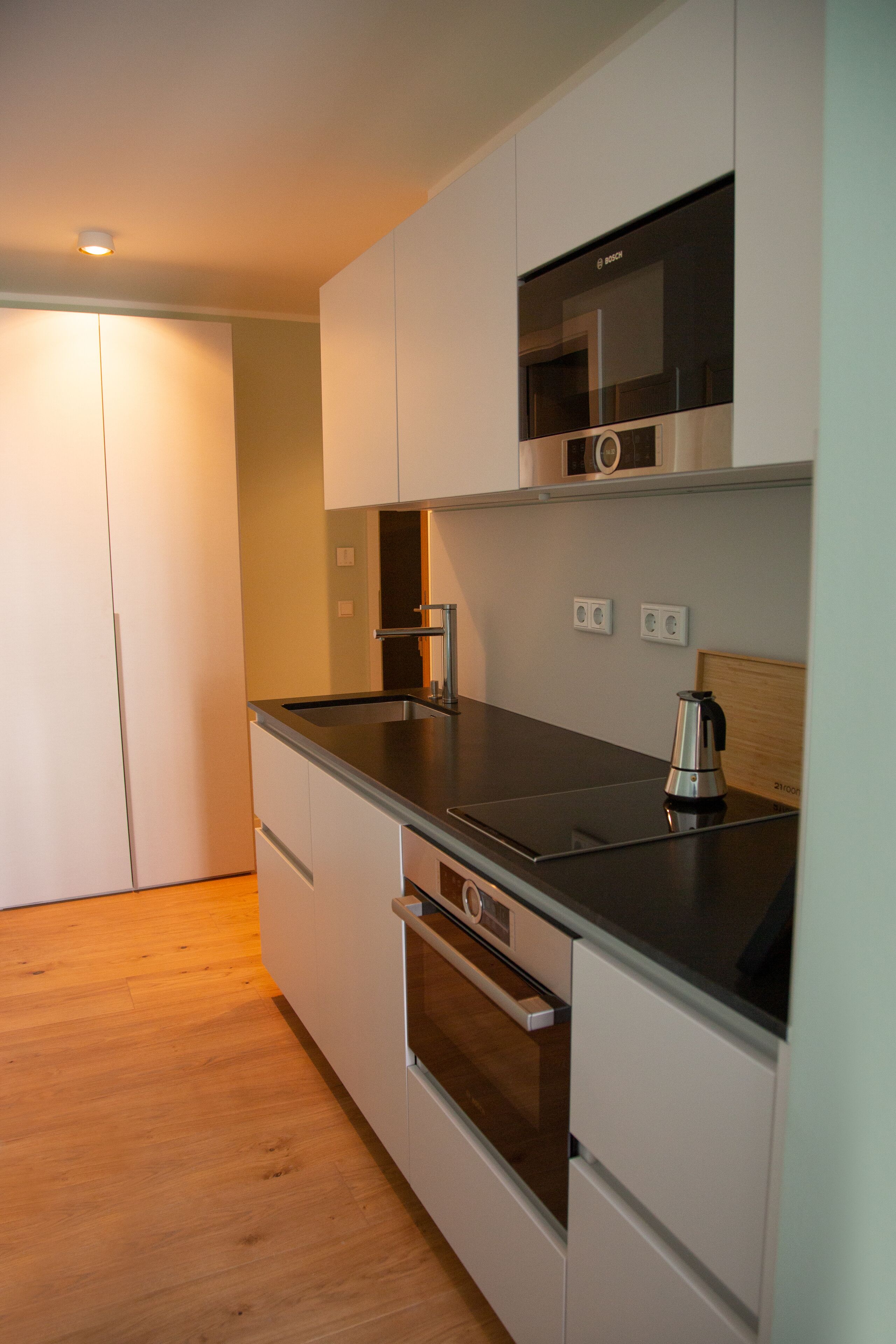 Cocina moderna con armarios blancos, encimera negra y electrodomésticos de acero inoxidable, incluyendo un microondas y un horno.