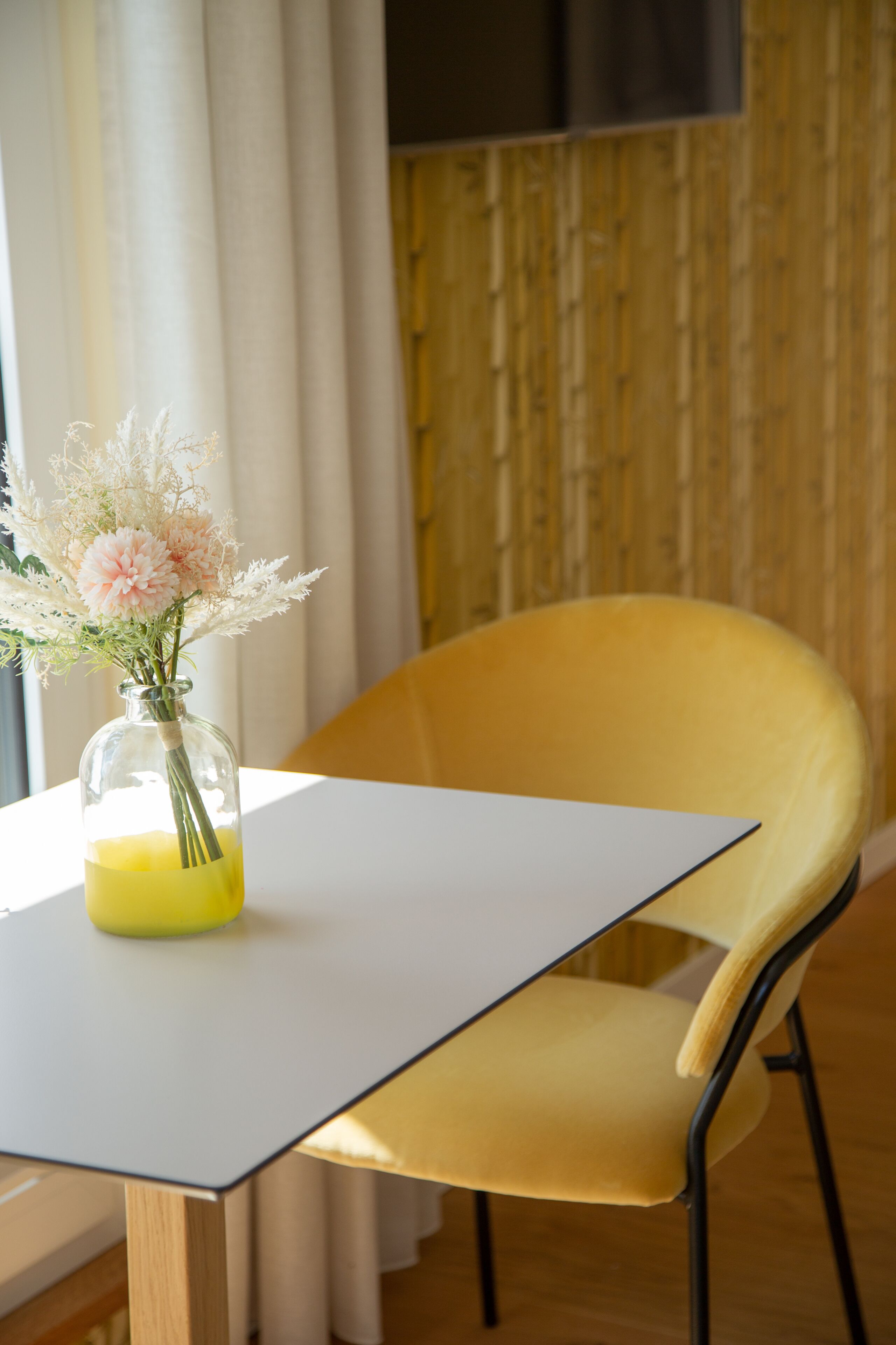 Ein Tisch mit Blumen in einer Vase, ein gelber Stuhl und ein Holzboden.