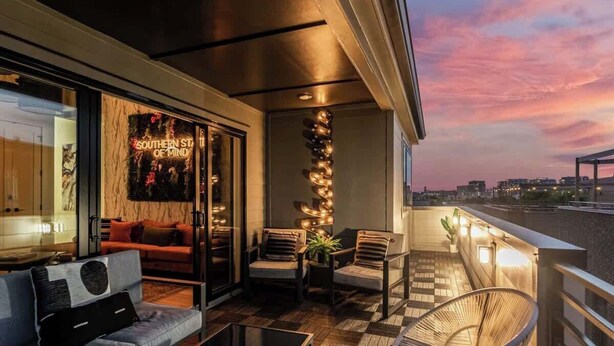 Ein Balkon mit Schachbrettmuster, zwei Stühle, eine Couch und ein Neonzeichen mit der Aufschrift 'SOUTHERN ST. OF MIND'.