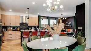 Eine moderne Küche mit Holzschnitzereien, einer zentralen Kochinsel und einem Essbereich mit rundem Tisch und grünen Stühlen.