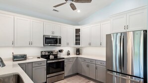 A modern kitchen with white cabinets, stainless steel appliances, and a wooden floor. - Tranquility Cove: New Build, Elevator, Pool Access (Nags Head)