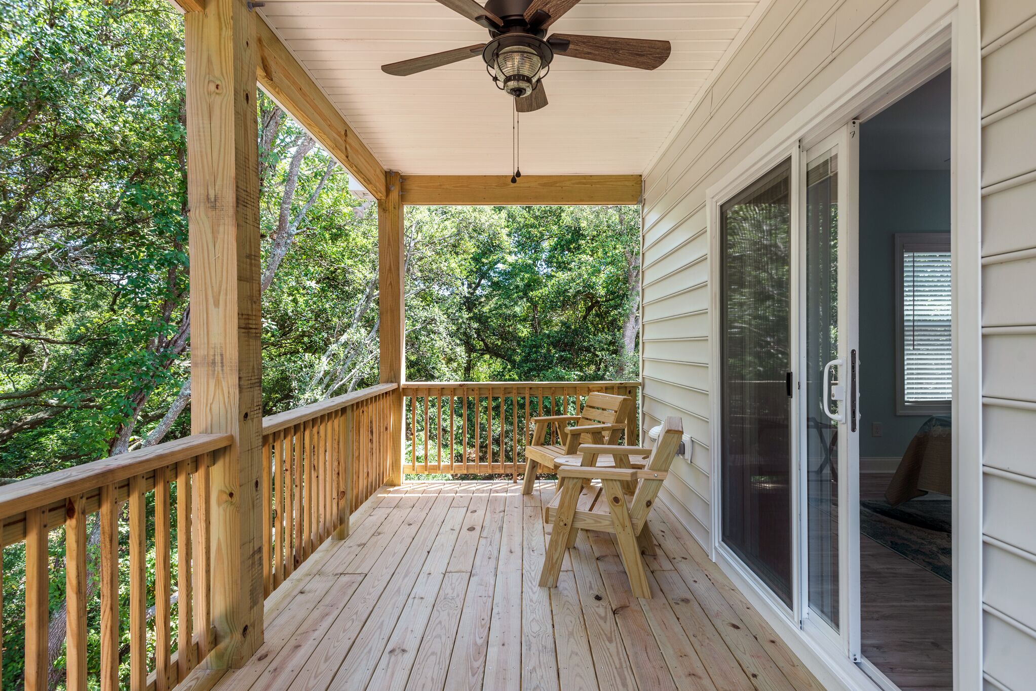A wooden deck with a ceiling fan, a sliding glass door, and a view of trees.