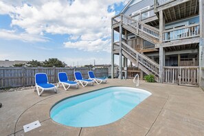 Ein Swimmingpool mit blauen Liegestühlen, einer Holzterrasse und einer mehrstöckigen Holzkonstruktion mit Balkonen.