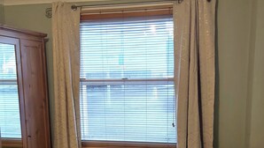 A room with a wooden cabinet, a small table with a decorative item, a cushioned chair with a patterned pillow, and a window with blinds.