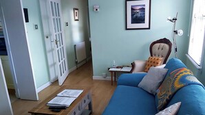 A living room with a blue sofa, a wooden coffee table with papers, a radiator, a framed picture on the wall, and a window with blinds.