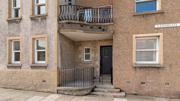 A two-story building with a stone facade, a balcony with a metal railing, and a door labeled "CANONGATE".