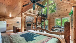 Ein rustikales Holzblockhaus-Interieur mit Bett, Kamin, Essbereich und Wendeltreppe.