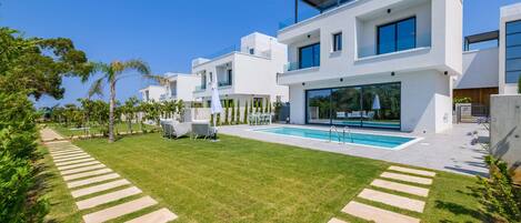 A modern two-story house with a swimming pool, a well-maintained lawn, and a clear blue sky.