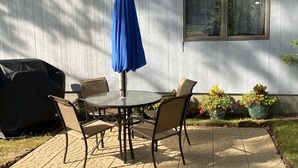 Terassi, jossa on pyöreä pöytä ja neljä tuolia, sininen aurinkovarjo ja grilli.