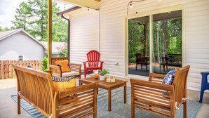 Eine überdachte Terrasse mit Holzmöbeln, einem roten Adirondack-Sessel und einer Glastür, die zu einer Außenterrasse führt.