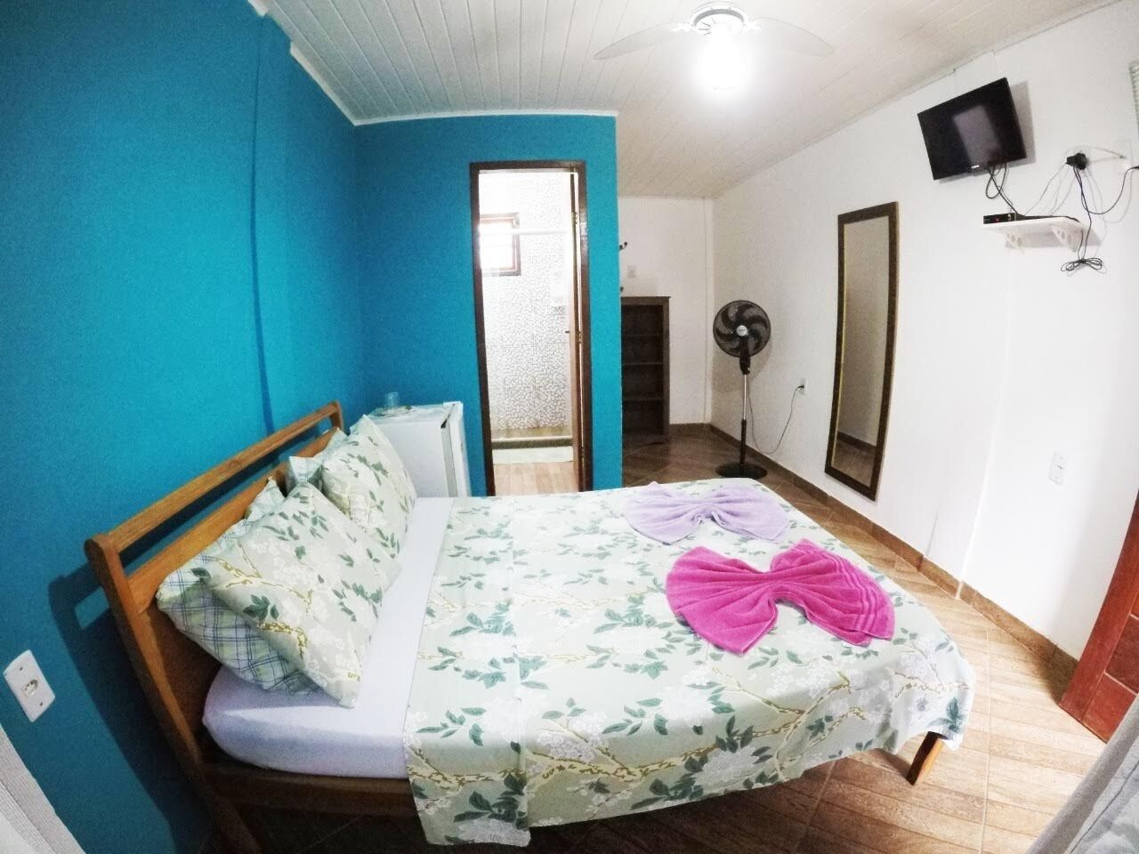 A bedroom with a wooden bed, a blue wall, a fan, a TV, and a mirror.