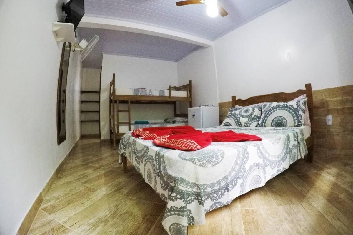 Een kleine kamer met een stapelbed, een plafondventilator, een bureau en een koelkast.