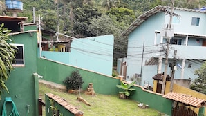 A residential area with a green wall, a tiled roof, and various potted plants. - Suítes Cantinho da Pedra (Angra dos Reis)