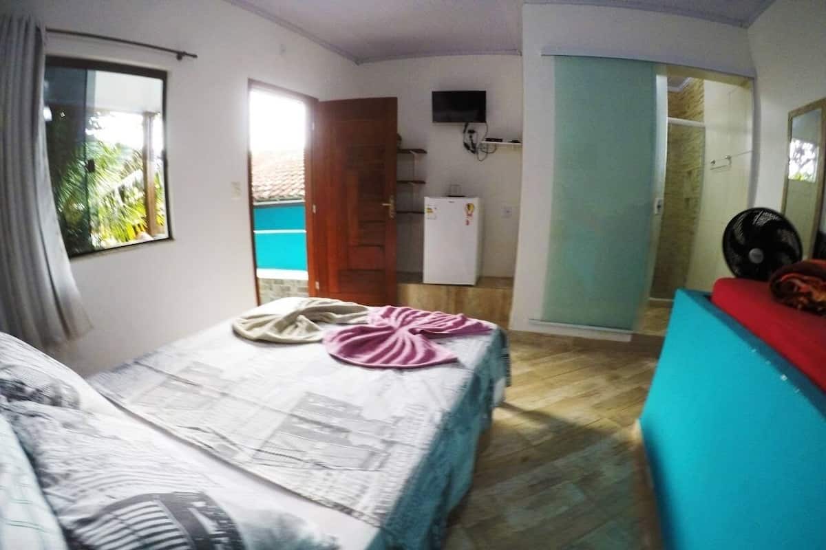 Een kamer met een bed, een tafeltje, een televisie en een ventilator.
