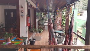 A cozy room with a wooden ceiling, a hammock, a fire extinguisher, and a colorful table. - Suítes Cantinho da Pedra (Angra dos Reis)