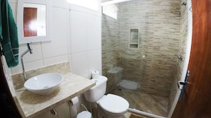 A bathroom with a white sink, two toilets, and a glass shower enclosure. - Suítes Cantinho da Pedra (Angra dos Reis)