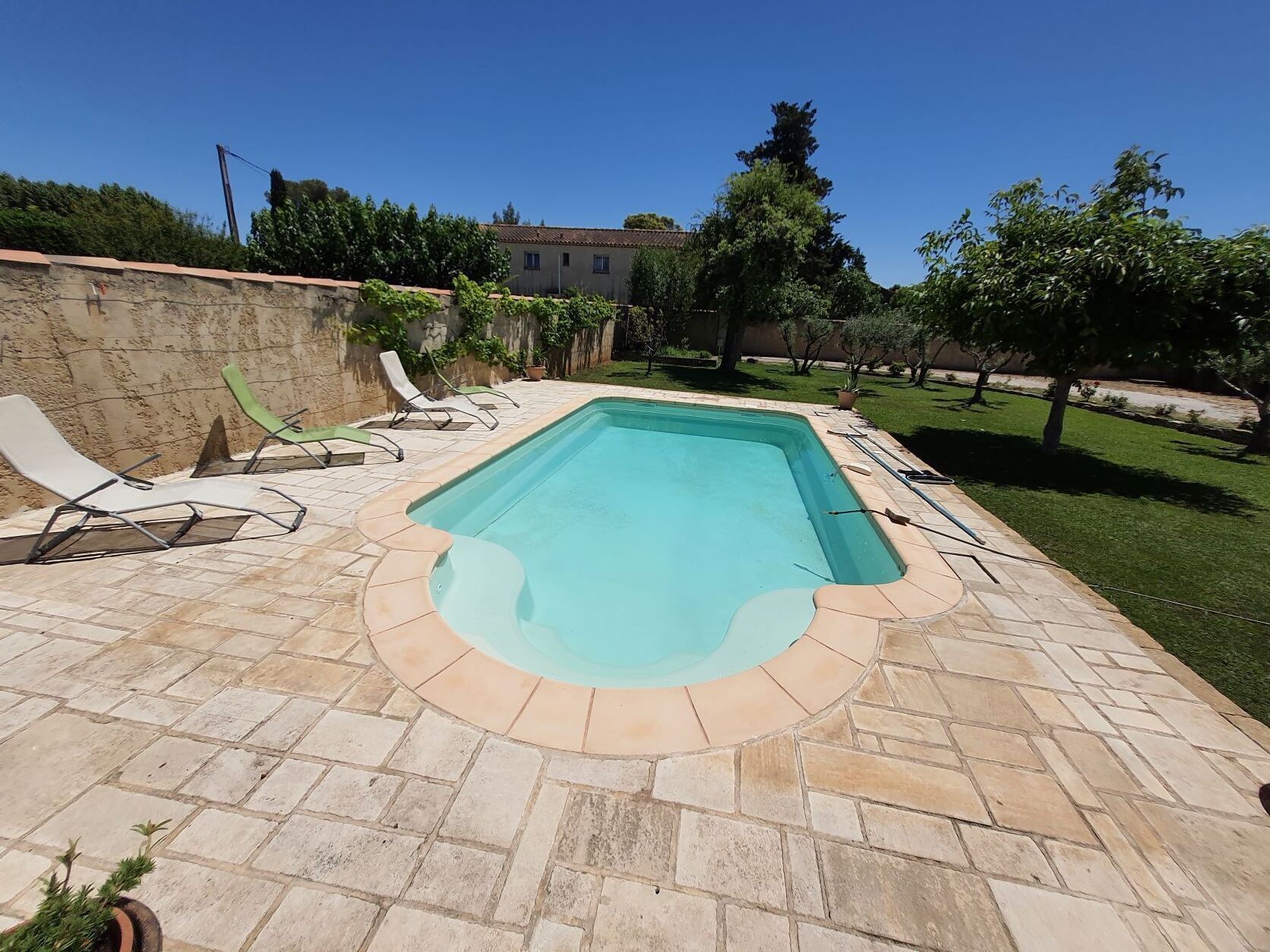 A rectangular swimming pool with a stone border, surrounded by a stone patio.