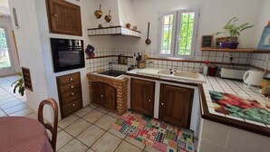 Een keuken met houten kastjes, een zwarte oven, een betegelde spatwand, een raam met uitzicht en een kleurrijk vloerkleed.