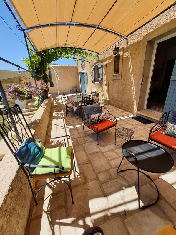A covered outdoor seating area with tables and chairs, a pergola with climbing plants, and a stone wall.
