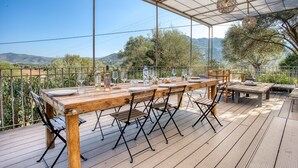 An outdoor dining area with a wooden table and chairs, set against a scenic backdrop of hills and trees.