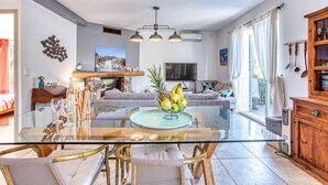 A modern living room with a glass dining table, wicker chairs, a sofa, and a TV.