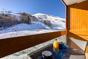 Un balcón con una mesa preparada para el desayuno, con vistas a un paisaje montañoso nevado, pistas de esquí y un telesilla.