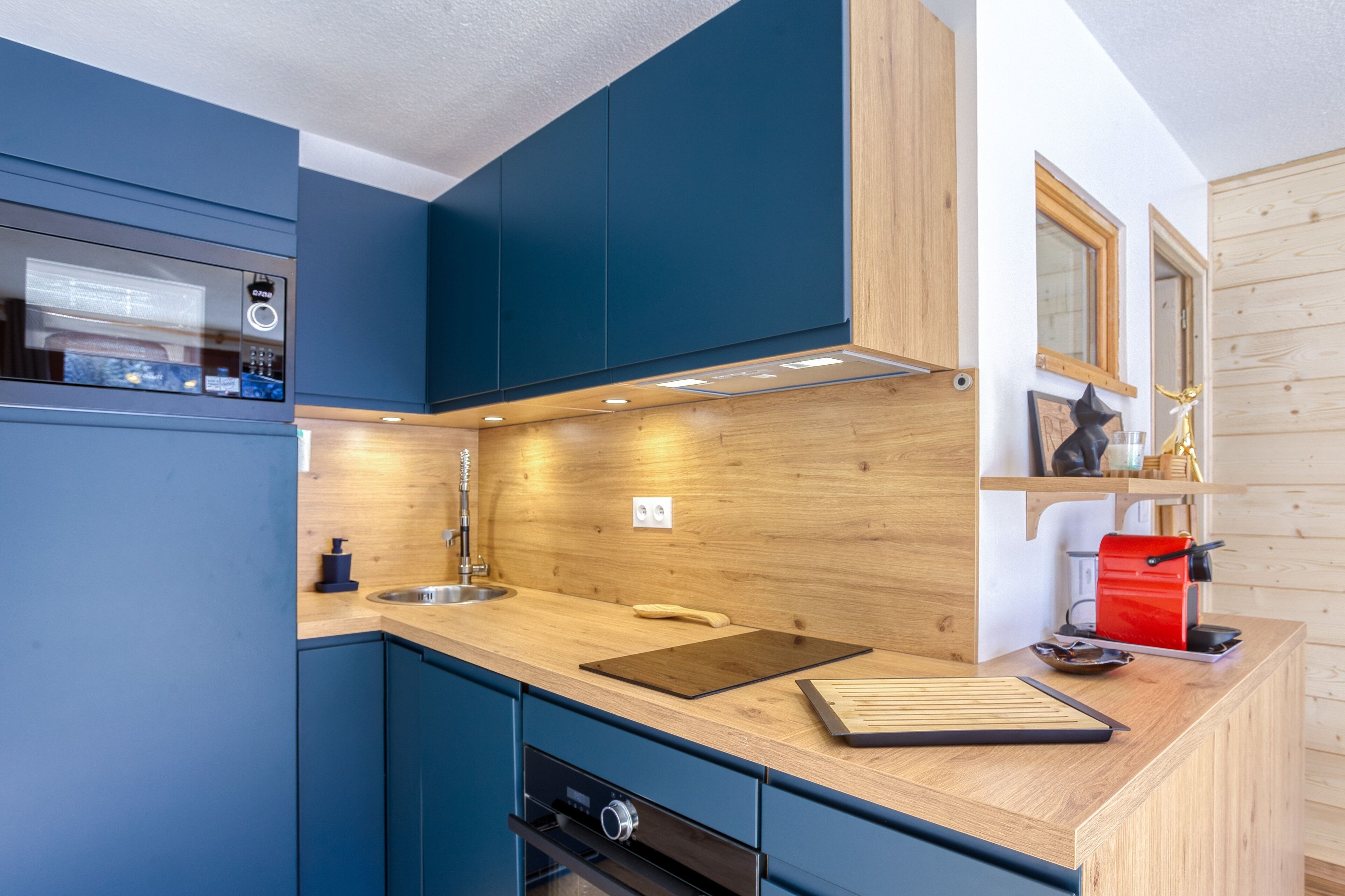 Una cocina moderna con armarios azules, encimera de madera y un tostador rojo.