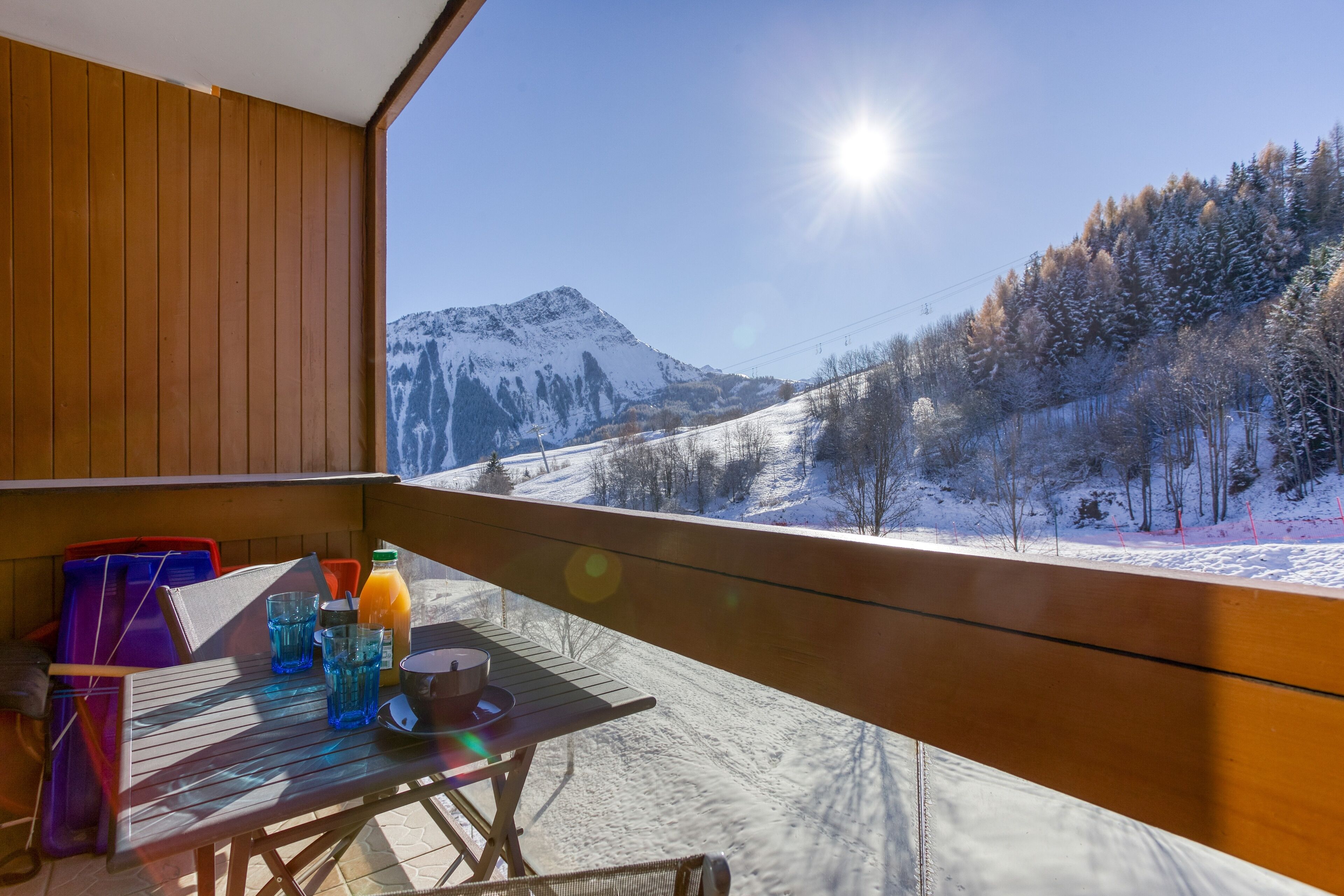 A wooden deck with a table and chairs, overlooking a snowy mountain landscape.
