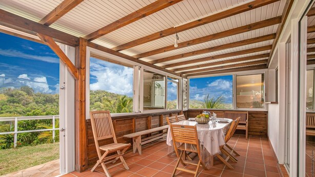 Een overdekt terras met houten meubels, een tafel en uitzicht op het landschap.