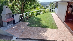 Eine Terrasse mit Steinplattenboden, einem Grill und einem weißen Zaun.