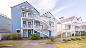 A multi-story residential building with a spiral staircase, balconies, and a well-maintained lawn. - Danou - Appartement avec Terrasse (Courseulles-sur-Mer)