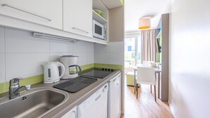 A modern kitchen with white cabinets, a microwave, a kettle, and a dishwasher. - Danou - Appartement avec Terrasse (Courseulles-sur-Mer)